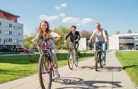 Smiling long-haired little girl with father and mother during summer city outdoor bicycle riding. They enjoy togetherness, happy parenthood and childhood or active sport life concept image