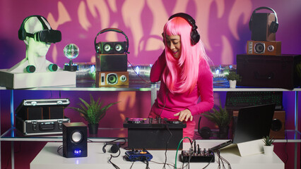 Musician with headphones standing at dj table dancing and having fun while mixing stereo sounds with electronics. Cheerful artist enjoying to perform music using professional turntables in nightclub