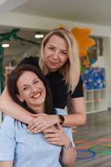 Two women share a heartfelt embrace while at a preschool, showcasing the nurturing and supportive...