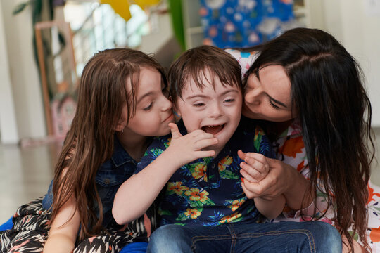 A girl and a woman hug a child with down syndrome in a modern preschool institution
