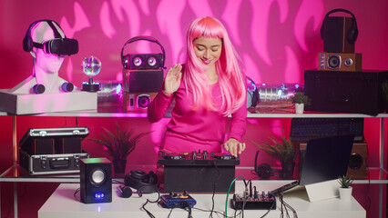 Asian performer dancing and interacting with fans in club at nightime, playing electronic remix at professional mixer console. Artist with pink hair mixing sounds using audio equipment