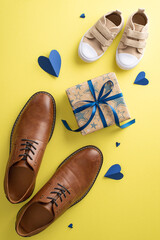 A heartwarming Father's Day tribute featuring vertical top view of tiny son and daddy's leather shoes, hearts, and gift box with bow on a yellow background