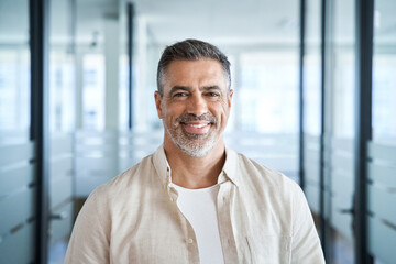 Headshot close up portrait of indian or latin confident mature good looking middle age leader, ceo male businessman on blur office background. Handsome hispanic senior business man smiling at camera. - obrazy, fototapety, plakaty