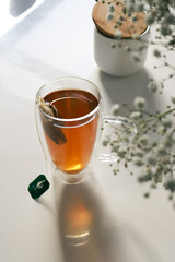 black tea in a glas cup on white table and flowers, blurred background 
