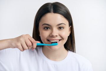 Headshot of a cute teenager girl brushing teeth with toothbrush, isolated on white studio background