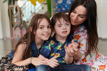A girl and a woman hug a child with down syndrome in a modern preschool institution