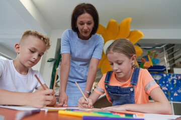 Creative kids during an art class in a daycare center or elementary school classroom drawing with female teacher.