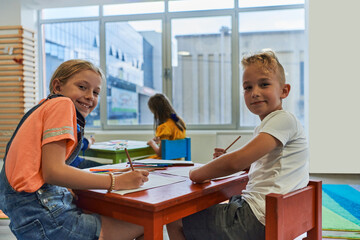 Cute girl and boy sit and draw together in preschool institution