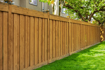 Nice new wooden fence around house. Wooden brown fence with green grass lawn. Street photo