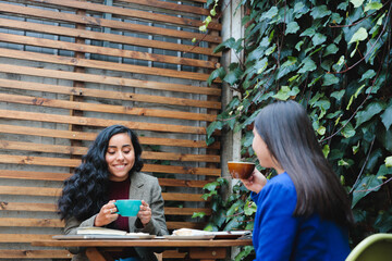 Two Young Latin Businesswomen Friends Enjoying Coffee on a Charming Cafe Patio, Embracing Success and Friendship