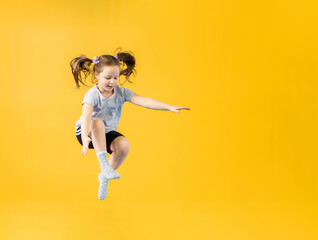 Fototapeta na wymiar Happy little girl jumping on yellow background