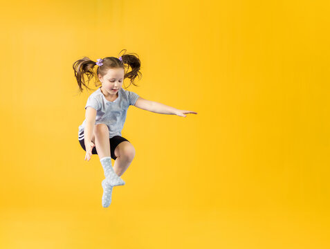 Happy little girl jumping on yellow background