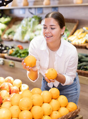 Obraz premium Happy smiling woman making purchases in supermarket, choosing fresh ripe oranges