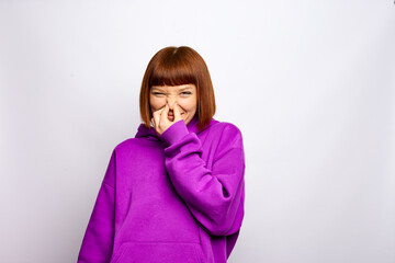 A woman in a purple hoody is closing her nose in reason of the smell.