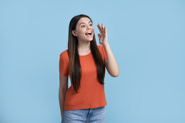 Obraz na płótnie Canvas Smiling positive Caucasian teenage girl holding hand near her face, shouting over blue background