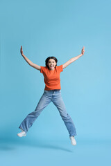 Full size portrait of a beautiful teenager girl smiles at camera and jumps over blue background