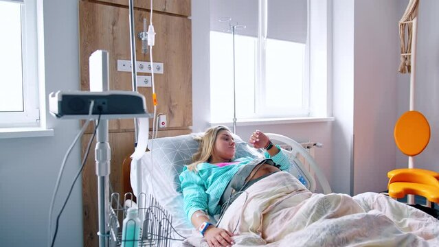 Pregnant blonde Caucasian woman lies in the hospital bed connected to equipment. Cardiotocography belt is on the belly of patient.