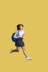 Fototapeta na wymiar Happy teenage student girl smiles looking at camera, running and jumping on isolated yellow backdrop