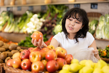 Pleased young woman customer taking ripe apples at the counter in large greengrocery