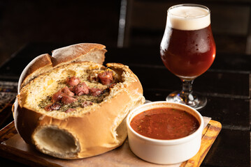 melted cheese fondue casserole on country bread with sausages and glass of beer on bar