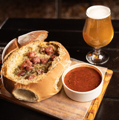 melted cheese fondue casserole on country bread with sausages and glass of beer on bar