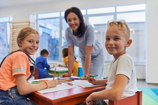 Creative kids during an art class in a daycare center or elementary school classroom drawing with female teacher.