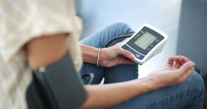 Closeup, blood pressure monitor and woman in home, living room and test hypertension, measure and data reading on device for healthcare. Girl, first aid and care for chronic medical issue or illness
