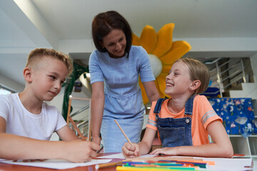 Creative kids during an art class in a daycare center or elementary school classroom drawing with female teacher.