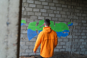 One young guy drawing graffiti on wall with spray can and mask on his face during the day	
