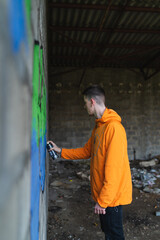 One young guy drawing graffiti on wall with spray can and mask on his face during the day	
