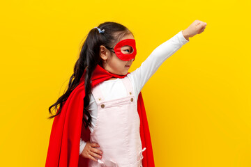 little asian girl in superman costume and mask shows with her hand forward and flies, korean child in superhero cape