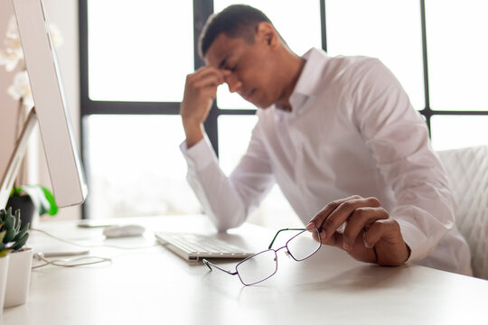 headache, african-american man takes off and holds glasses and wipes his closed eyes, office worker guy has sore eye