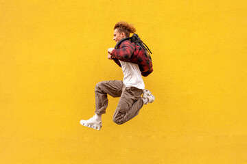 young cheerful guy student with backpack quickly runs in the air and jumps against yellow isolated wall