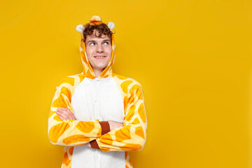 young pensive guy in funny baby giraffe pajamas dreams and thinks on yellow background, man in animal clothes