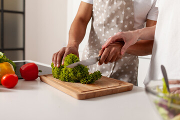 multiracial young couple preparing veggie vegetable and greens salad in white modern kitchen