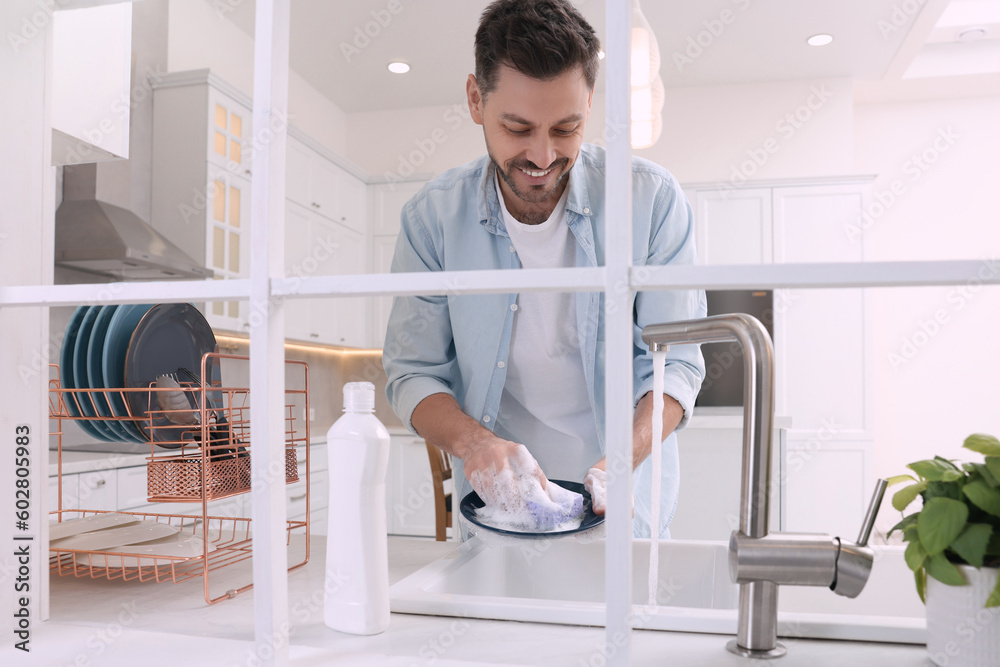 Canvas Prints Man washing plate above sink in kitchen, view from outside