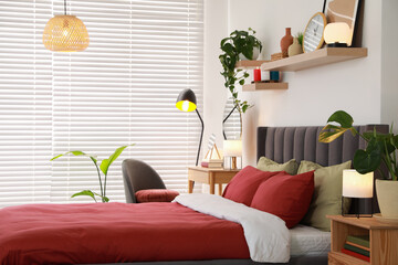 Stylish bedroom interior with comfortable bed, dressing table, lamps and green houseplants