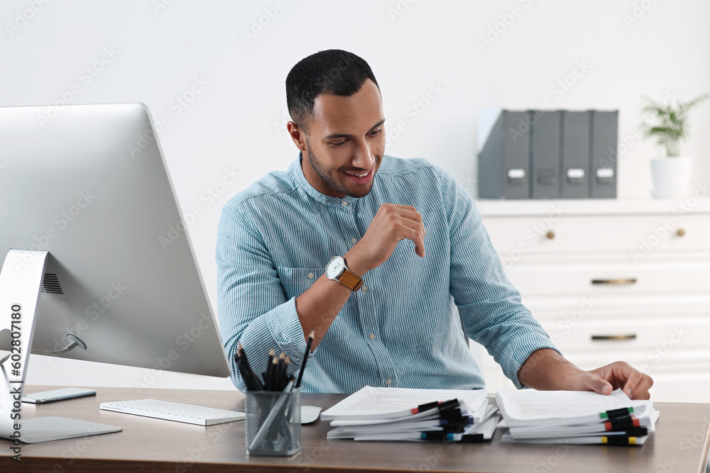 Wall mural Happy young businessman working with documents at wooden table in office