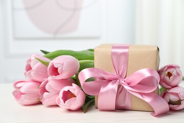 Beautiful gift box with bow and pink tulips on white table