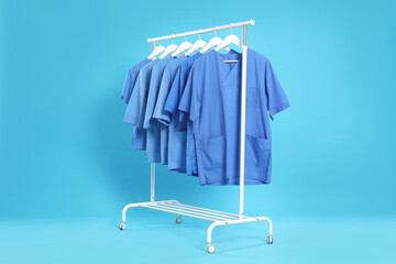 Medical uniforms on rack against light blue background