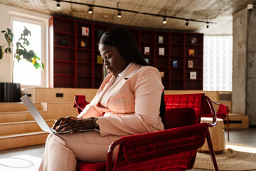 Young african american woman in suit using laptop at office lobby