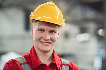 Portrait of smiling Caucasian professional heavy industry engineer wearing safety uniform and yellow helmet in industrial factory, blurred background.
