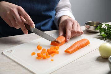 Woman cutting boiled carrot at white wooden table, closeup. Cooking vinaigrette salad