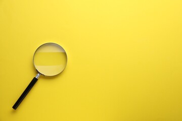 Magnifying glass on yellow background, top view. Space for text