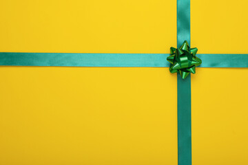 Green ribbons with bow on yellow background, top view. Space for text