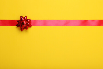 Red ribbon with bow on yellow background, top view. Space for text