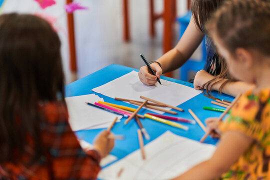 Close up photo of kids during an art class in a daycare center or elementary school classroom drawing with female teacher.