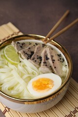 Bowl of delicious rice noodle soup with meat and egg on brown table, closeup
