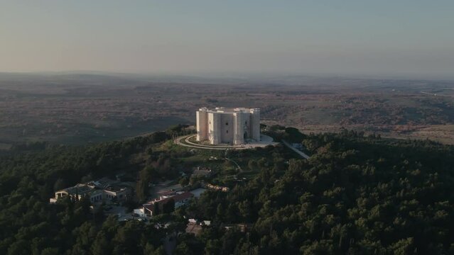 Aerial of a white 13th century Italian citadel on top of a hill and green forest in Puglia, Italy 4K drone