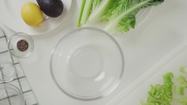 Chopped green celery in a glass bowl. Celery lettuce salad recipe, ingredients close-up on white background